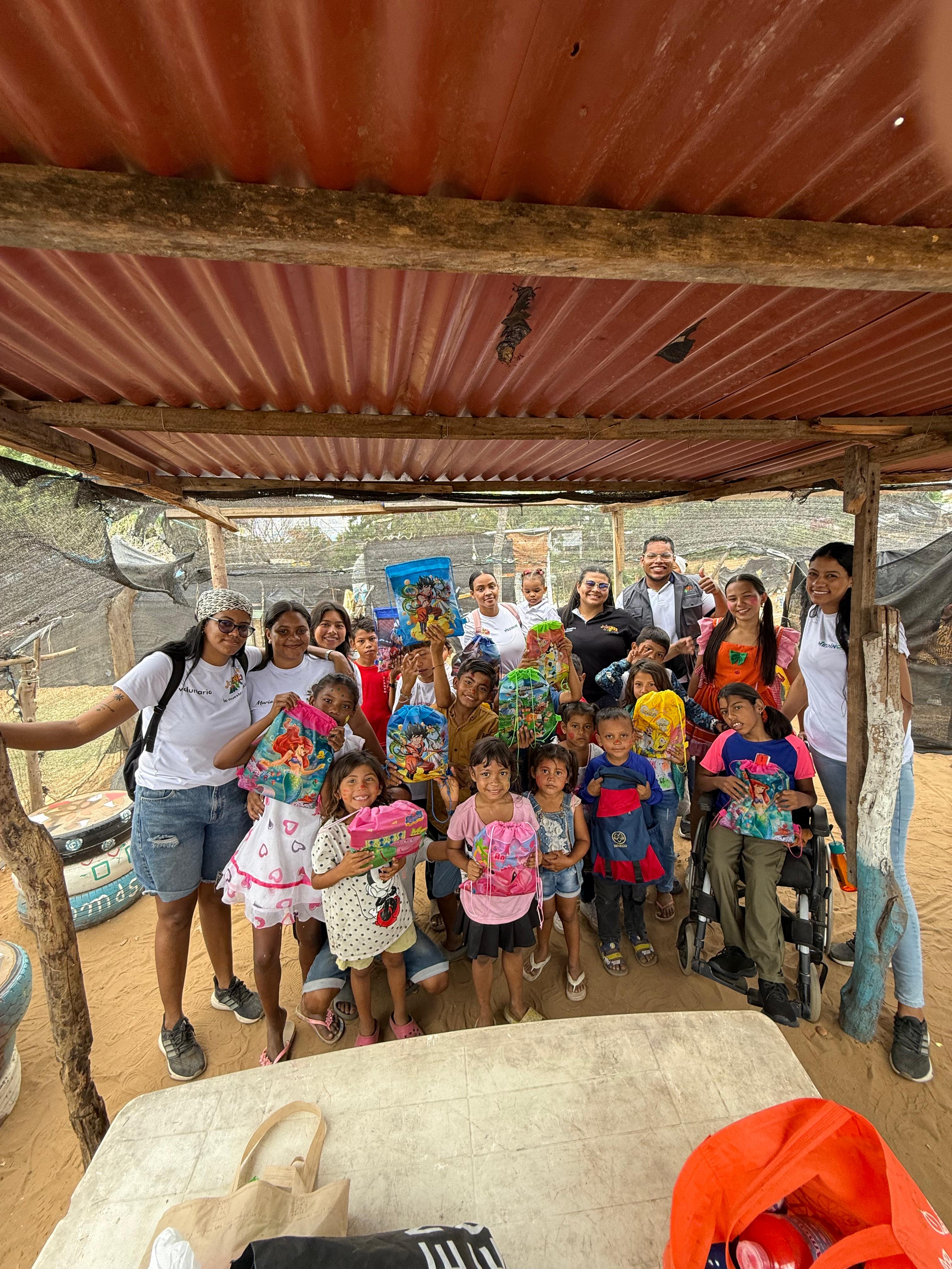 Voluntarias y voluntarios de la Corporación Jóvenes Maicao entregando kits escolares a niñas y niños en un barrio de Maicao